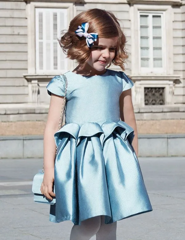 A little girl in a blue dress is standing in front of a building