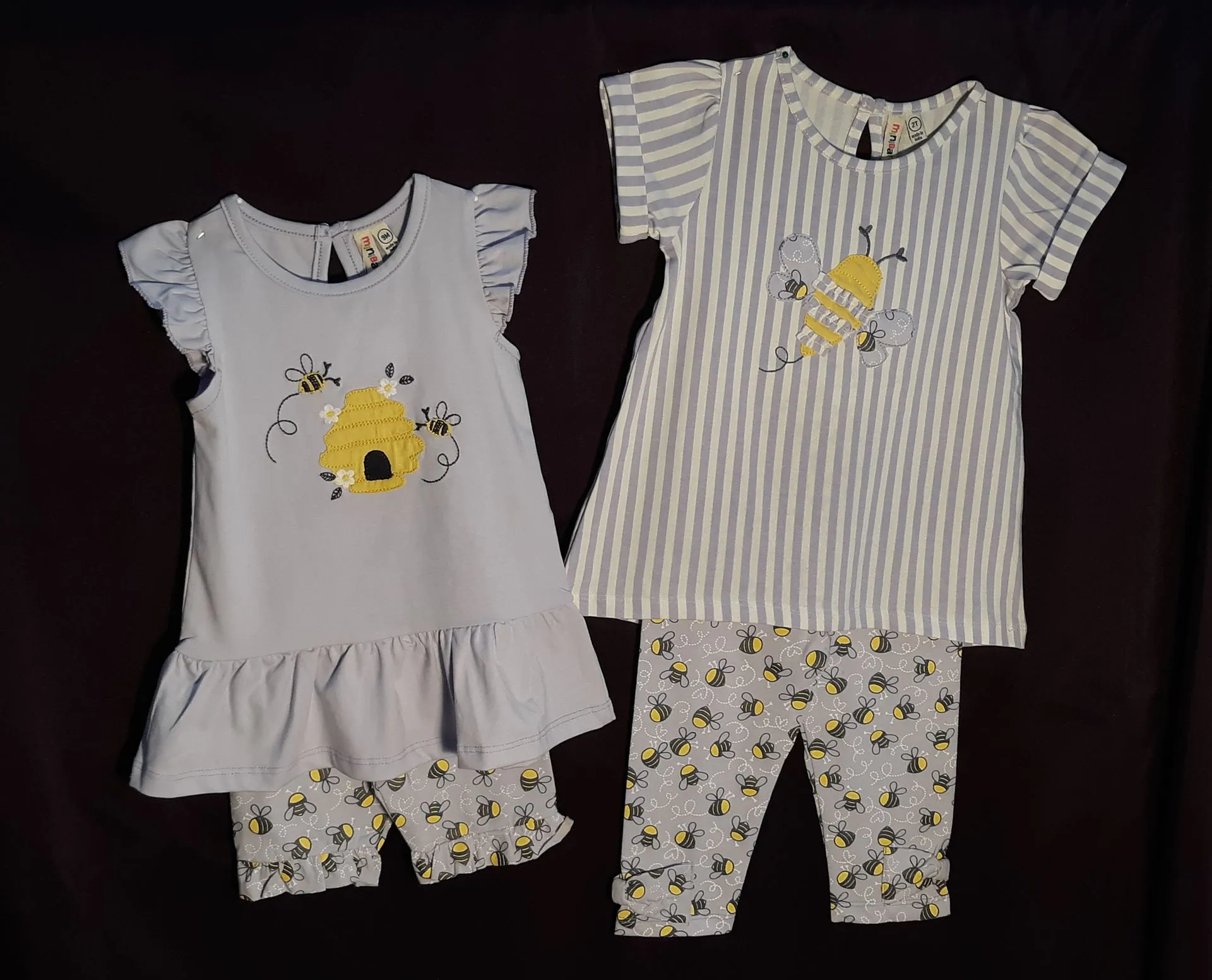 Two baby clothes with bees on them are sitting next to each other on a table.