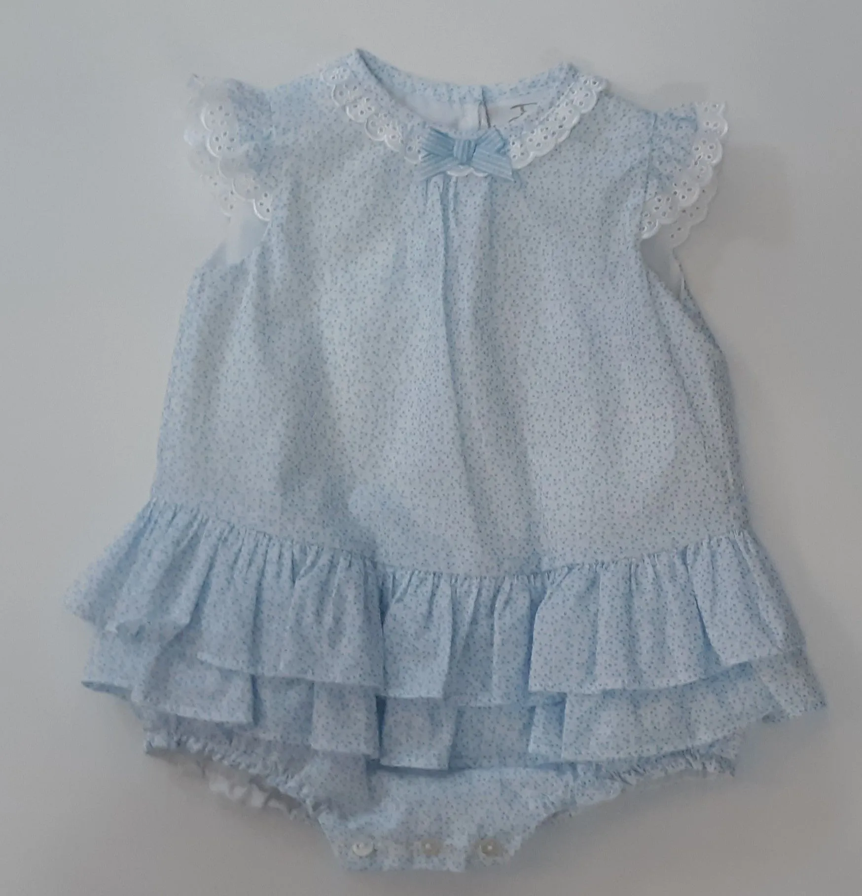 A baby girl is wearing a light blue dress with ruffles