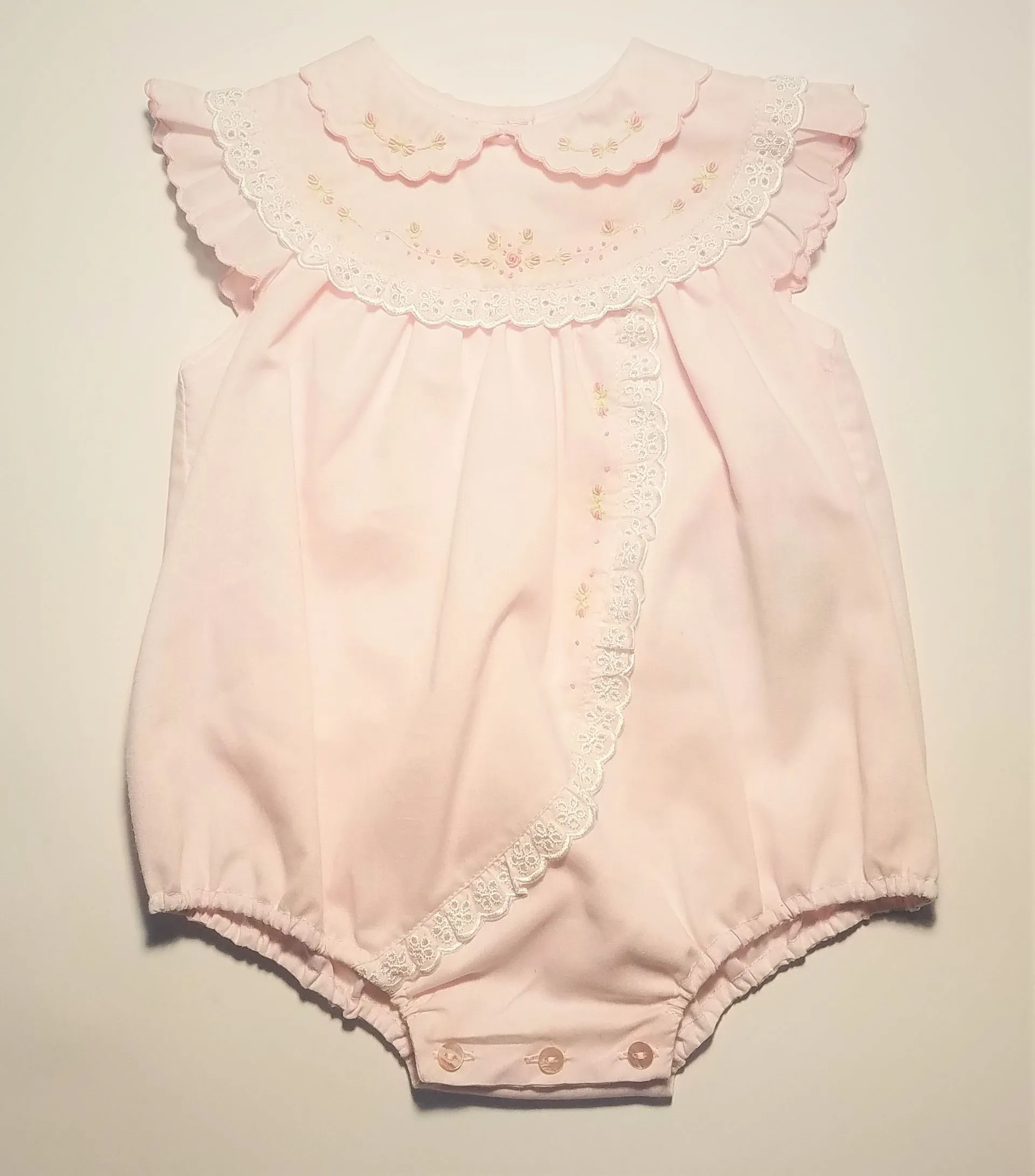 A baby girl is wearing a pink romper with white lace trim