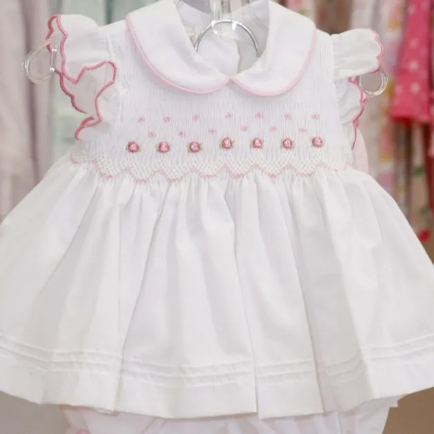 A white baby dress with pink embroidery is hanging on a hanger.