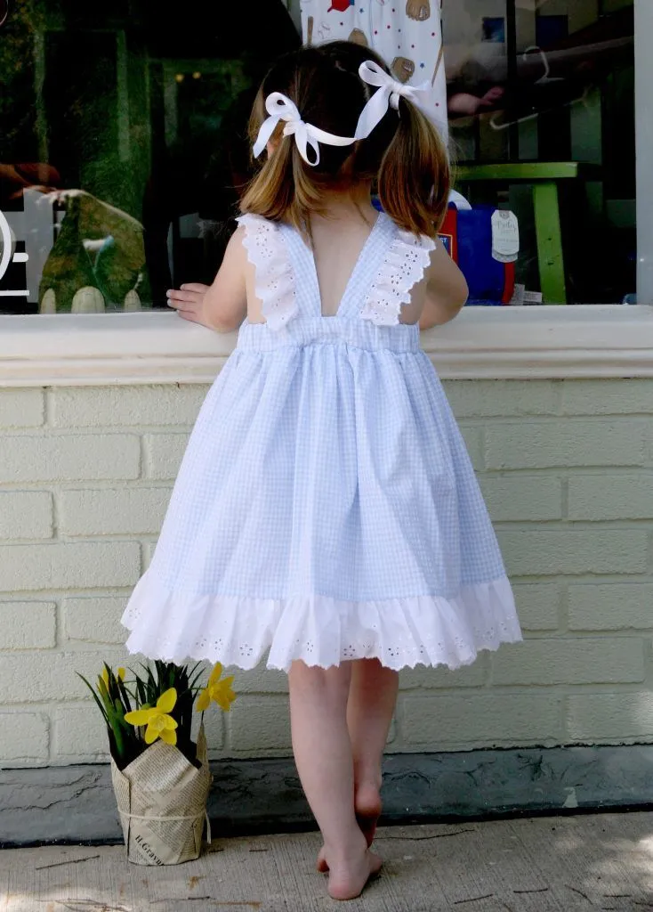 A little girl in a white dress stands in front of a window