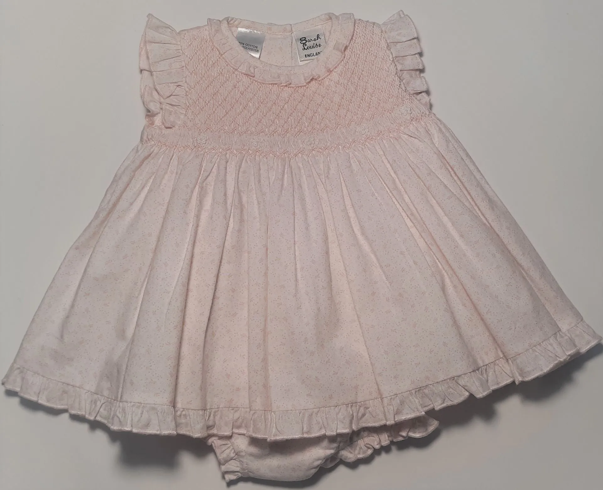 A baby girl is wearing a white dress and diaper cover