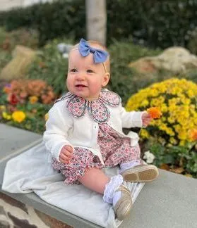 A baby girl is sitting on a bench holding a flower.