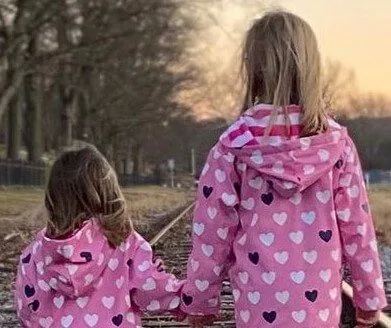 Two little girls are holding hands while standing on train tracks.